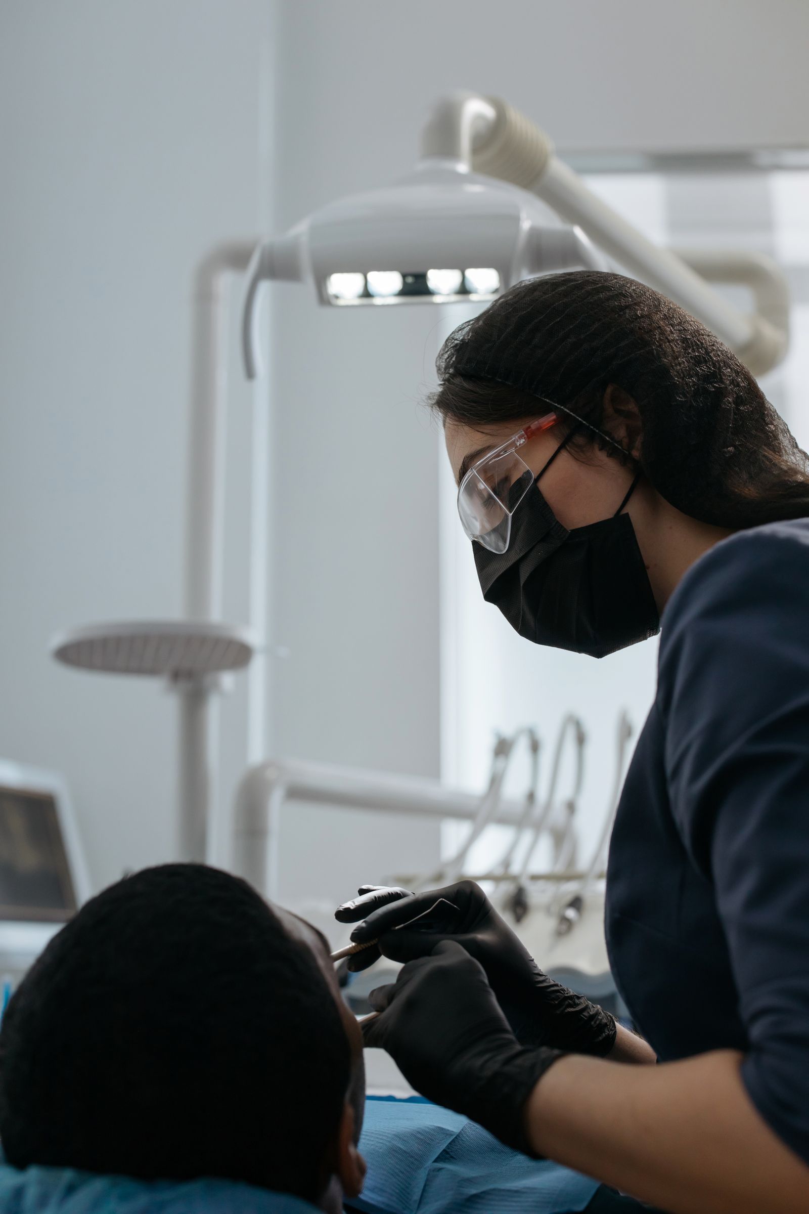 A dentist in dark scrubs working closely over a patient